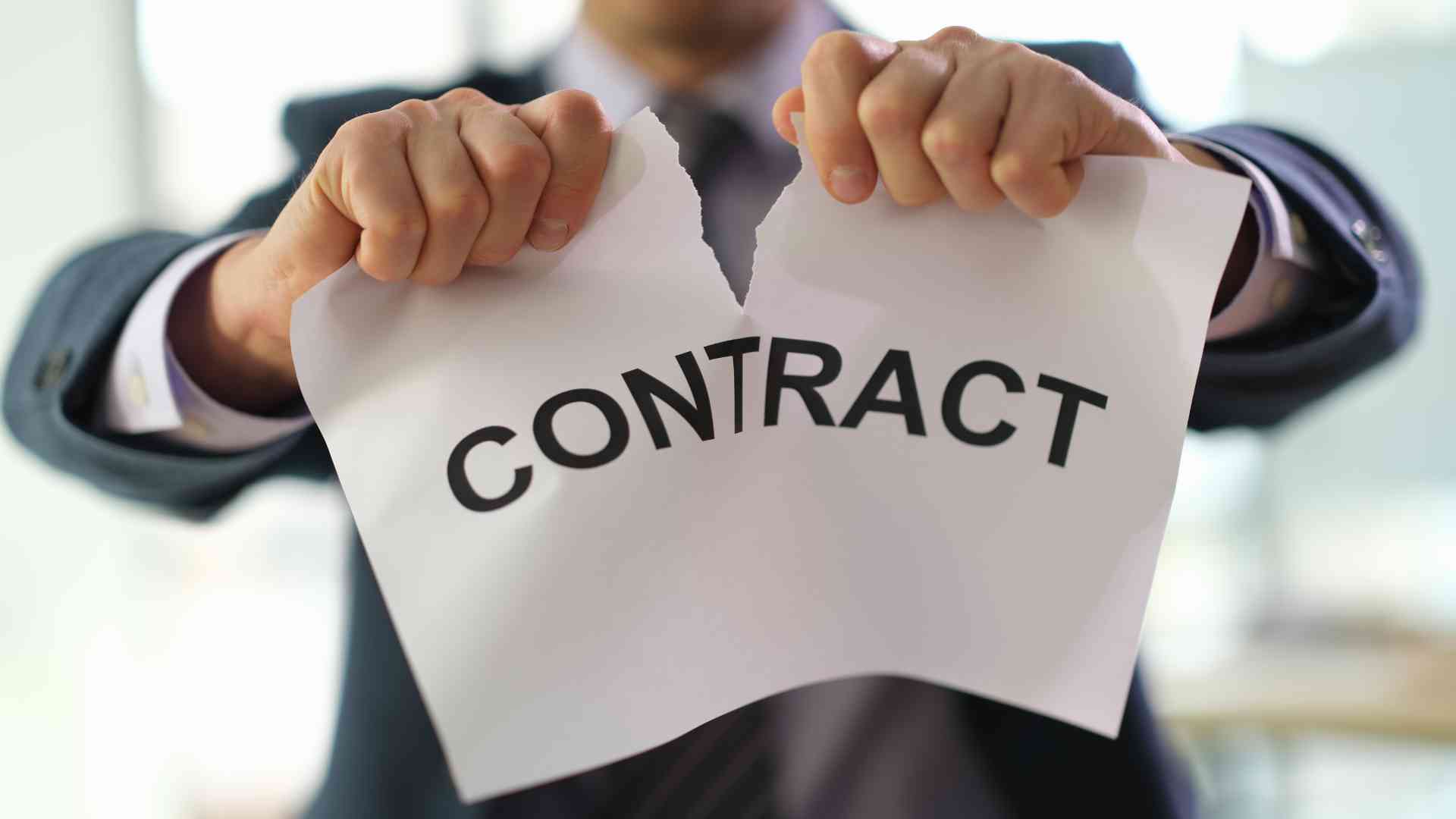 A hand ripping a contract in half, symbolizing the termination of a virtual assistant agreement.