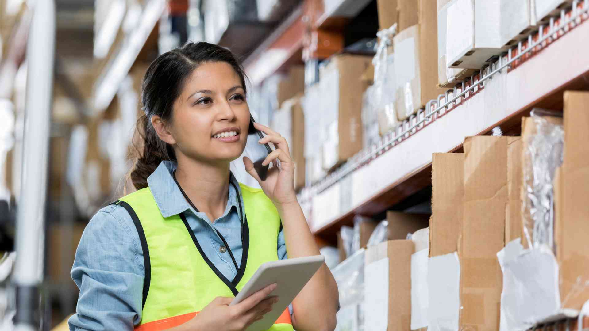 A woman in a warehouse calling someone and taking a look on the products, overall managing logistics.   