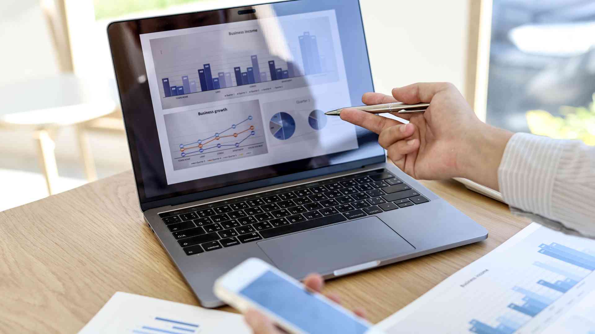 Person pointing at charts on a laptop screen, analyzing business data.